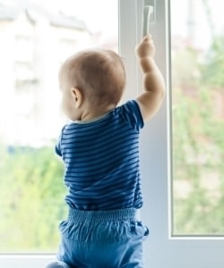 Image depicts a chhild standing in front of a window.