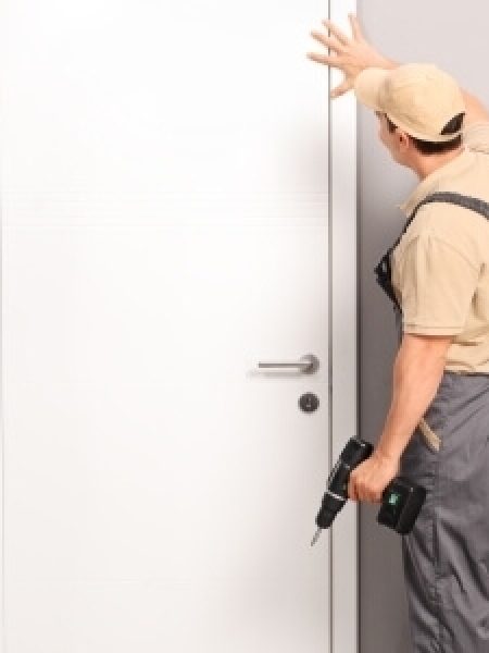 Image depicts handyman installing white door.