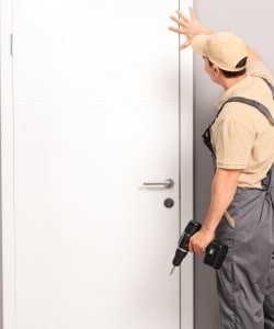 Image depicts handyman installing white door.