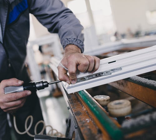 Image depicts a man manufacturing a vinyl window.