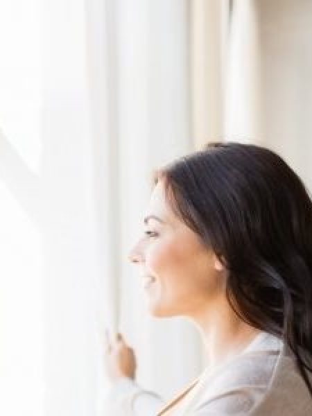 Image depicts a woman standing by her vinyl window.