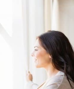 Image depicts a woman standing by her vinyl window.