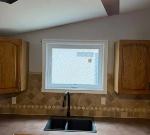White casement window above a kitchen sink between oak cabinets