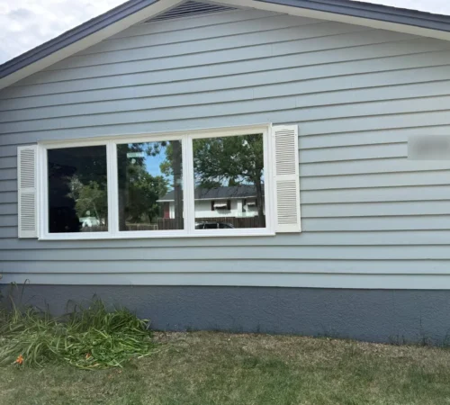 New white front window set between shutters on grey siding in Winnipeg